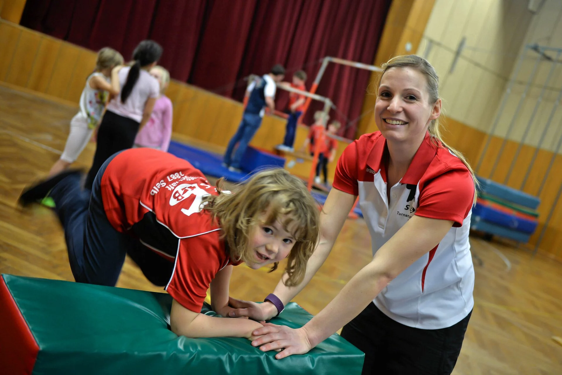 Übungsleiterin turnt mit Kindern in einer Sporthalle