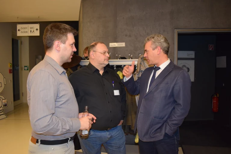 Drei Männer im Gespräch im Foyer, einer mit Trinkflasche in der Hand