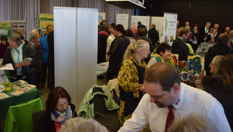 Besucherinnen und Besucher an Informationsständen in einem Veranstaltungsraum