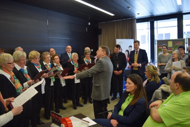 Chorleiter dirigiert singende Gruppe in Schals vor Publikum beim Aktionstag