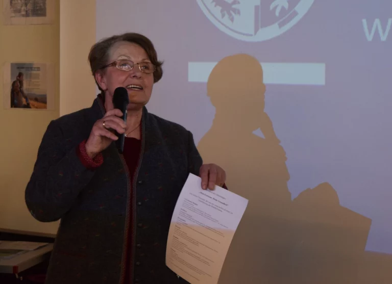 Frau mit Mikrofon spricht vor Publikum, im Hintergrund projizierte Präsentation
