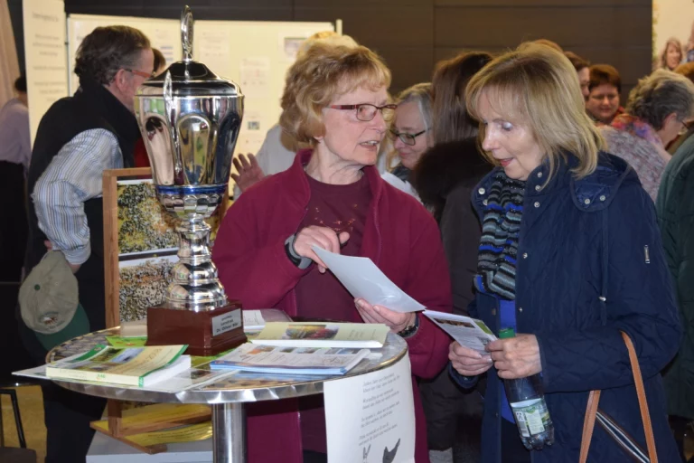 Besucherinnen informieren sich an einem Stehtisch mit Pokal und Broschüren beim Aktionstag