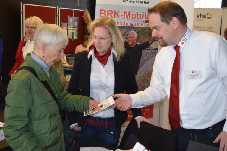 BRK-Mitarbeiter übergibt einer Besucherin Informationsmaterial am Messestand