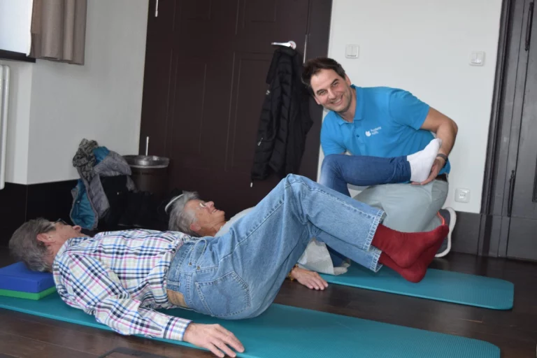 Physiotherapeut unterstützt eine Person bei einer Rückenübung auf einer Gymnastikmatte