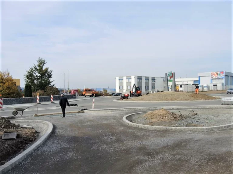Baustelle am Kreisverkehr mit Baggern, Materiallager und Person auf frischem Betonbelag