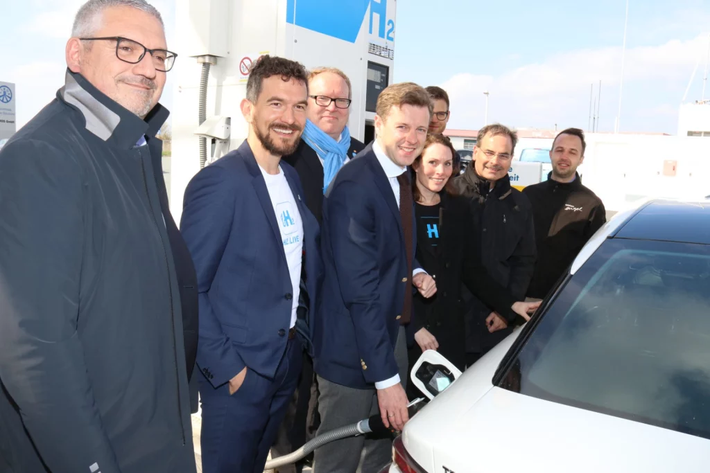 Gruppe von Personen vor der Wasserstofftankstelle beim Betanken eines Fahrzeugs