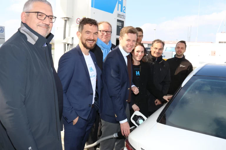 Gruppe von Personen vor der Wasserstofftankstelle beim Betanken eines Fahrzeugs