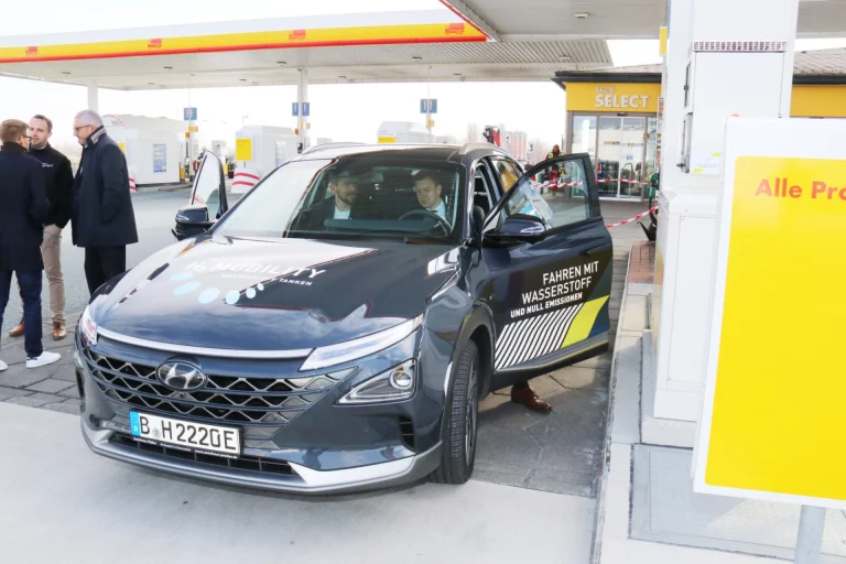 Männer begutachten wasserstoffbetriebenes Fahrzeug an der Tankstelle in Berg