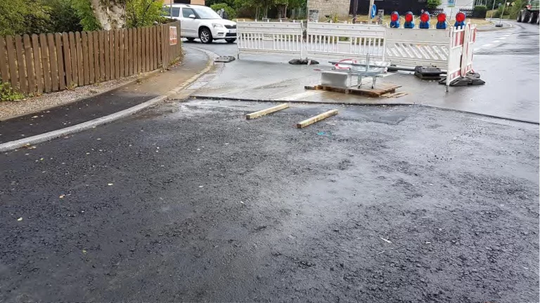 Aufgerissene Asphaltdecke einer Straße mit Absperrungen und Warnbaken an einer Kreuzung