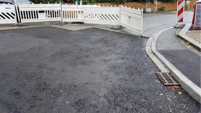 Neu asphaltierte Straßenfläche neben Absperrgittern und Gullydeckel in Döhlau