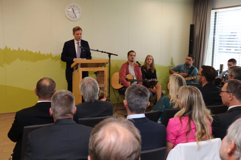 Mann am Rednerpult spricht bei einer Feier, im Hintergrund Musikband und Publikum