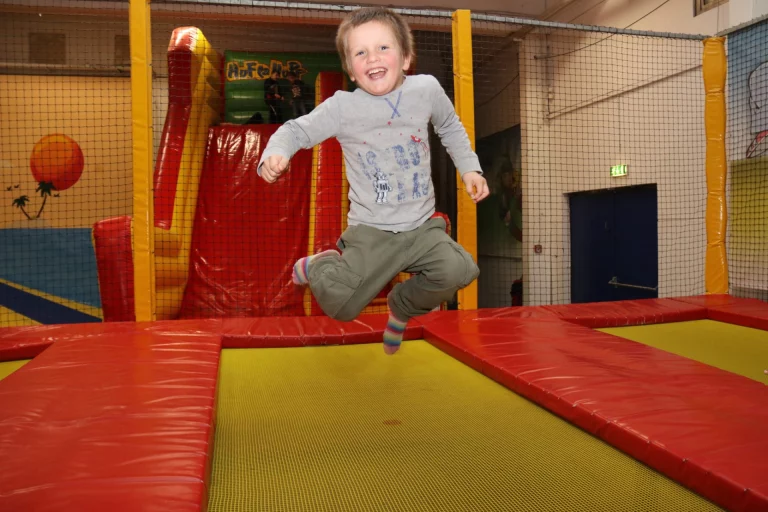 Kind springt lachend auf einer Hüpfburg in der Trampolinhalle