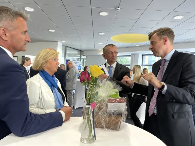 Vier Männer und eine Frau im Gespräch an einem Stehtisch mit Blumenstrauß