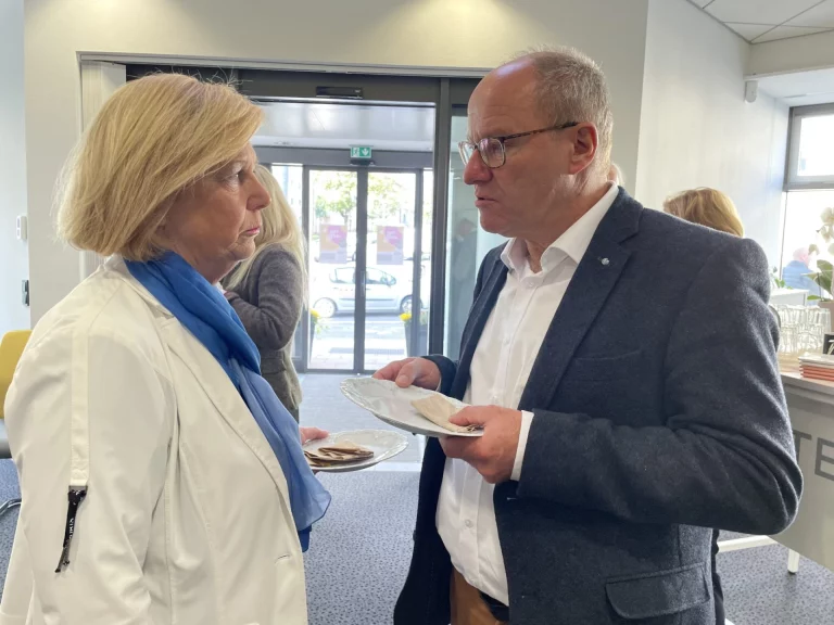 Staatsminister im Gespräch mit einer Frau im Eingangsbereich, beide mit Teller in der Hand