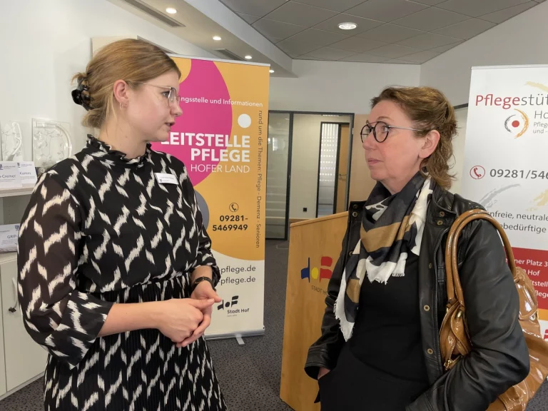 Zwei Frauen im Gespräch vor Roll-ups zur Leitstelle Pflege Hofer Land und zum Pflegestützpunkt