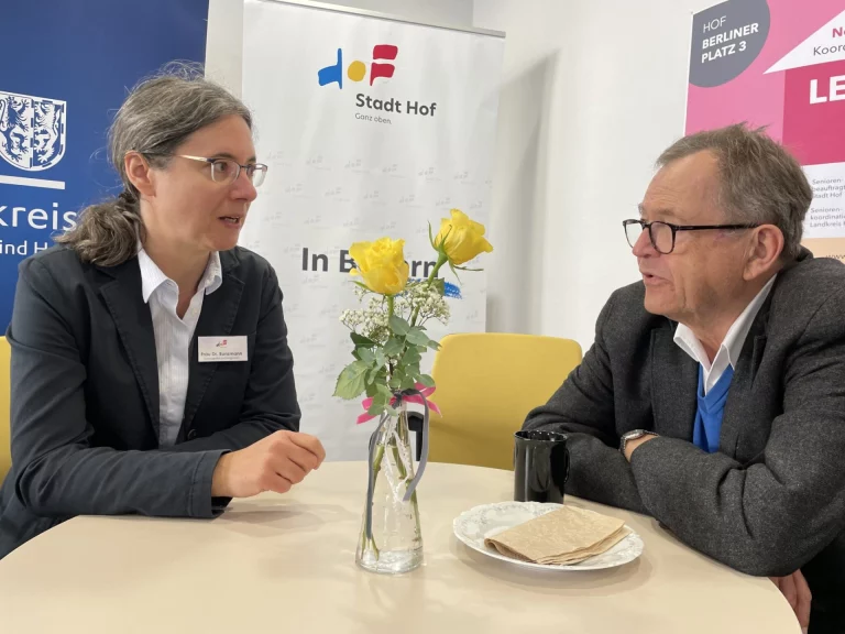 Frau und Mann im Gespräch an einem Tisch mit Blumenstrauß und Kaffee