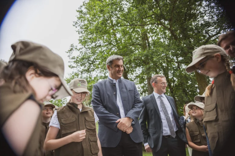 Ministerpräsident mit Begleitperson inmitten von Kindern in Rangerkluft im Freien