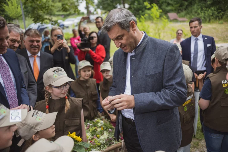 Markus Söder im Gespräch mit Kindern in Naturpark-Westen bei Blumenstrauß und Sonnenblume