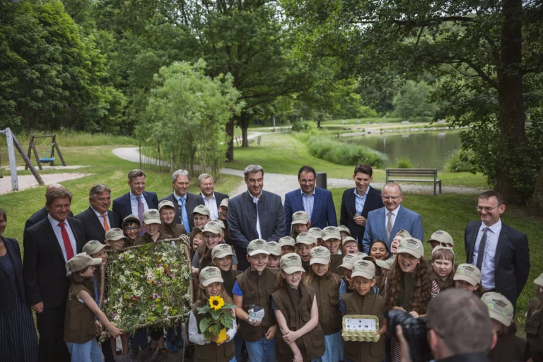 Ministerpräsident Söder mit Kindern in Rangerkleidung und weiteren Personen am Seeufer im Frankenwald