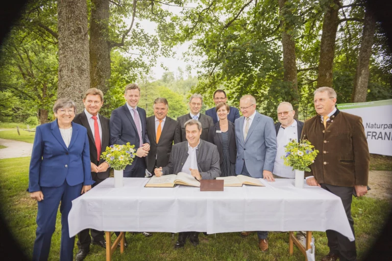 Dr. Markus Söder unterzeichnet Urkunde am Tisch, umgeben von Gruppe vor Naturpark-Frankenwald-Banner
