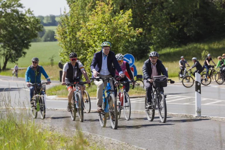Gruppe von Radfahrenden, vorn ein Mann im Anzug, auf einem neu angelegten Radweg mit Verkehrsschild