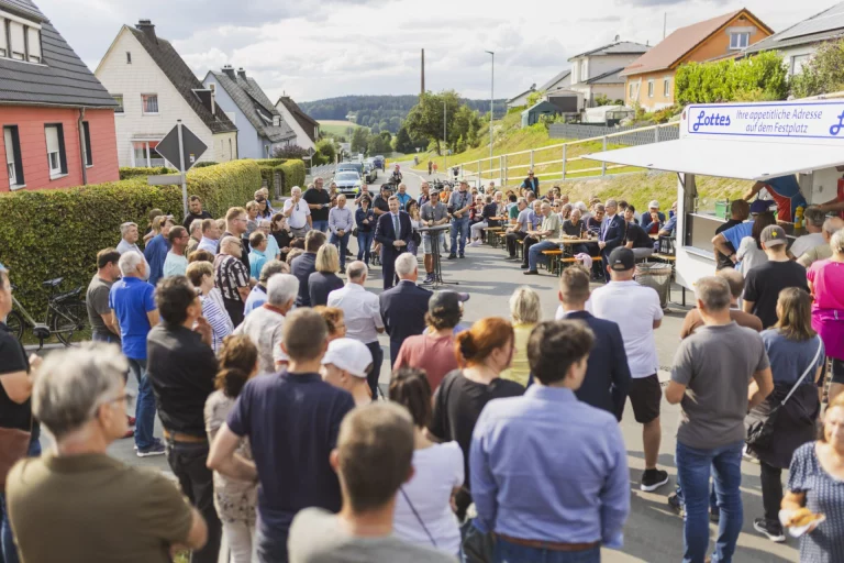 Menschenmenge bei Freiluftveranstaltung mit Rednerpult auf der Straße zwischen Ortschaften