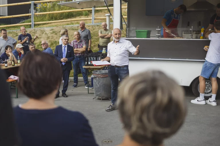 Mann hält Ansprache vor Imbisswagen, im Hintergrund wartende Gäste bei der Einweihungsfeier