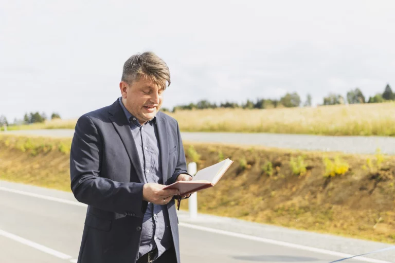Mann in Jackett liest an einer Landstraße aus einem Buch