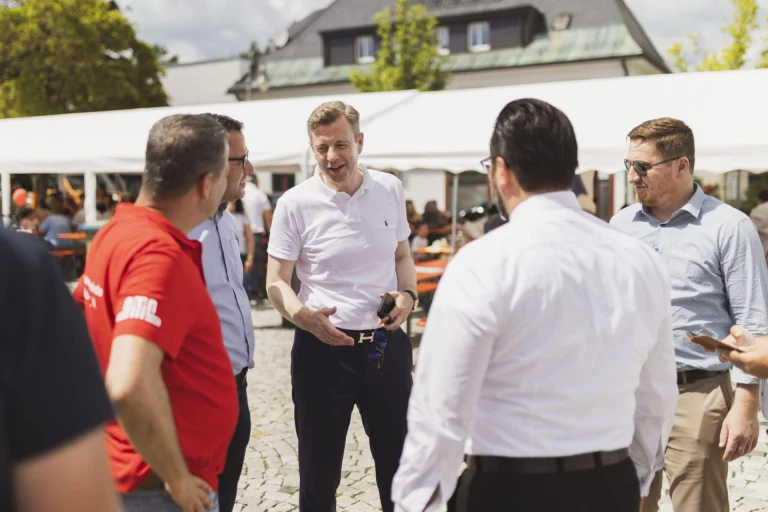 Mann im weißen Poloshirt spricht mit einer Gruppe von Personen vor einem Festzelt