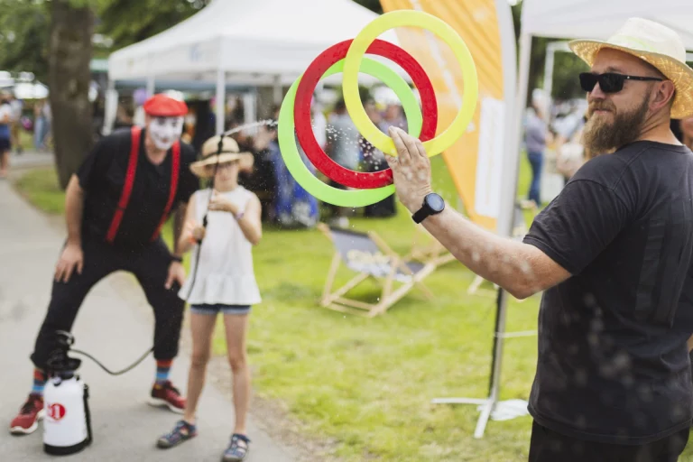 Pantomime besprüht Mädchen mit Wasser, Mann jongliert mit Ringen beim Fest im Park