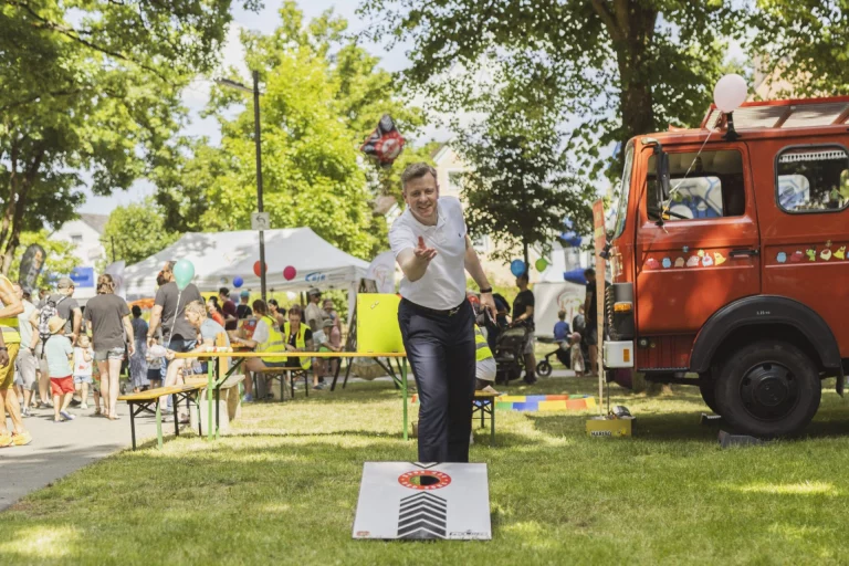 Mann wirft beim Cornhole-Spiel einen Sandsack, im Hintergrund Feuerwehrfahrzeug und Festbesucher