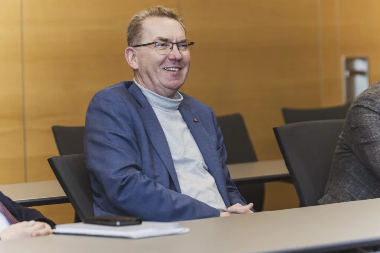 Mann im Sakko lächelt im Sitzungssaal während eines Gesprächs am Tisch