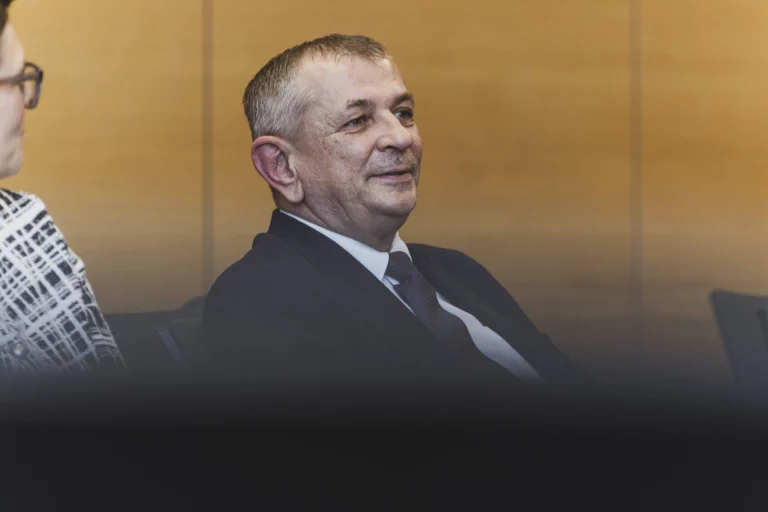 Mann im Anzug sitzt lächelnd bei einer Veranstaltung neben weiterer Person
