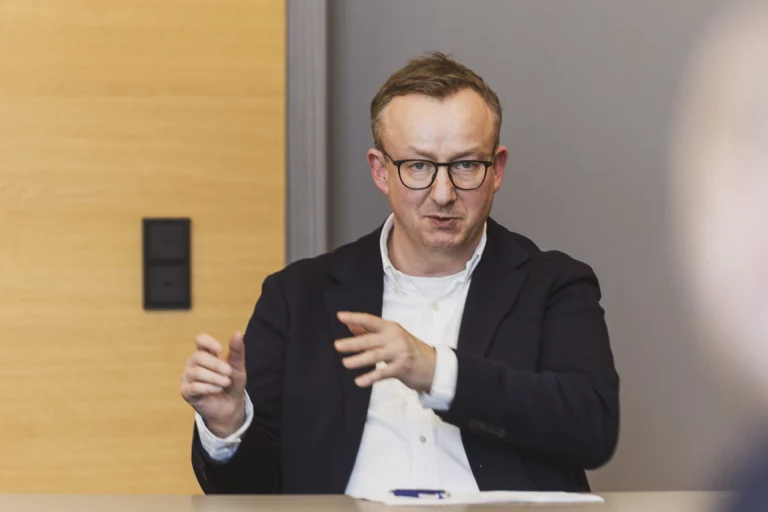 Mann mit Brille und dunklem Sakko gestikuliert während eines Gesprächs am Tisch