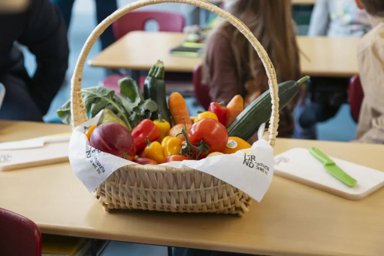 Korb mit frischem Gemüse und Obst auf einem Schultisch im Klassenzimmer