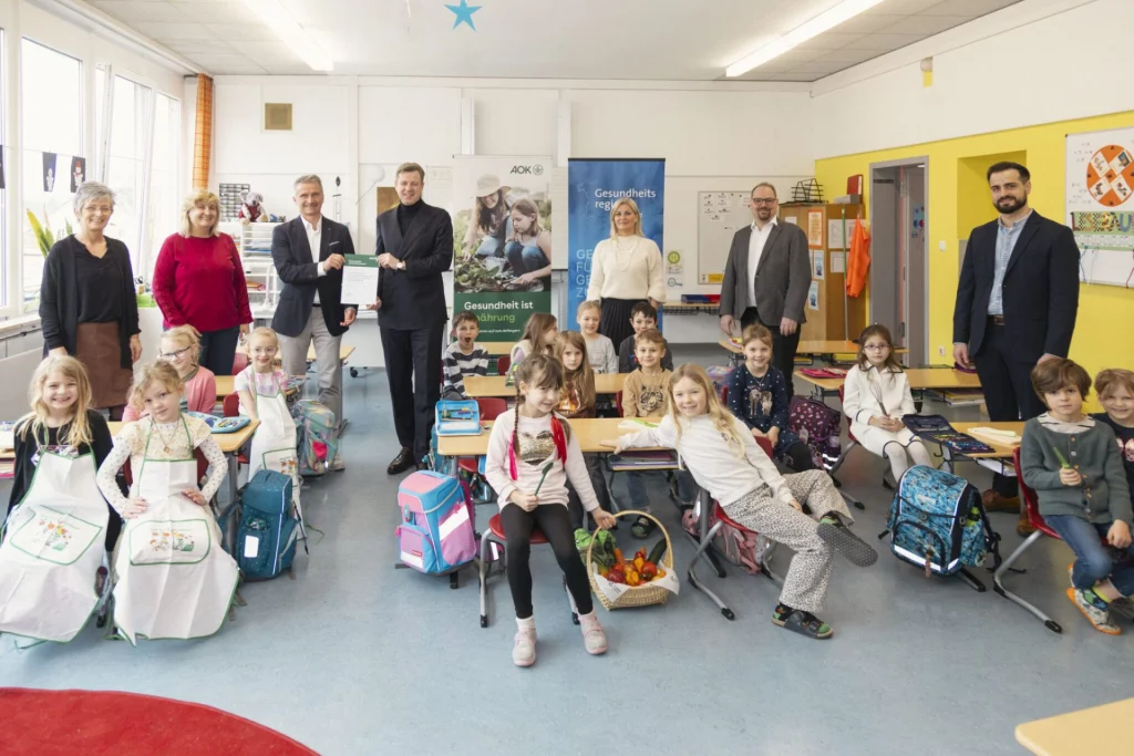 Gruppe von Erwachsenen und Schulkindern mit Pausenbroten und Schultaschen im Klassenzimmer
