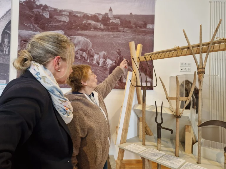 Zwei Frauen betrachten historische Fotografie und landwirtschaftliche Geräte in Museumsausstellung