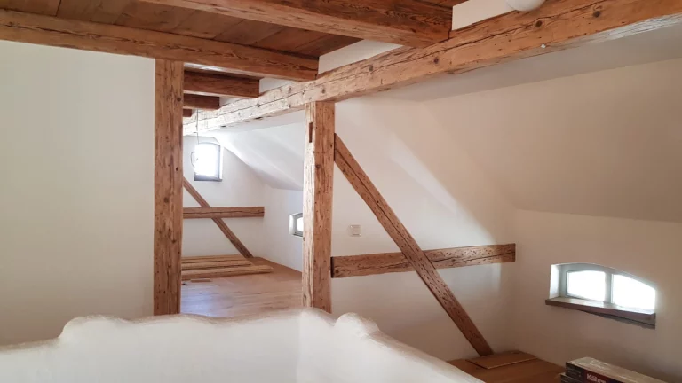 Dachgeschossausbau mit sichtbaren Holzbalken, sanierten Fensterlaibungen und weiß verputzten Wänden