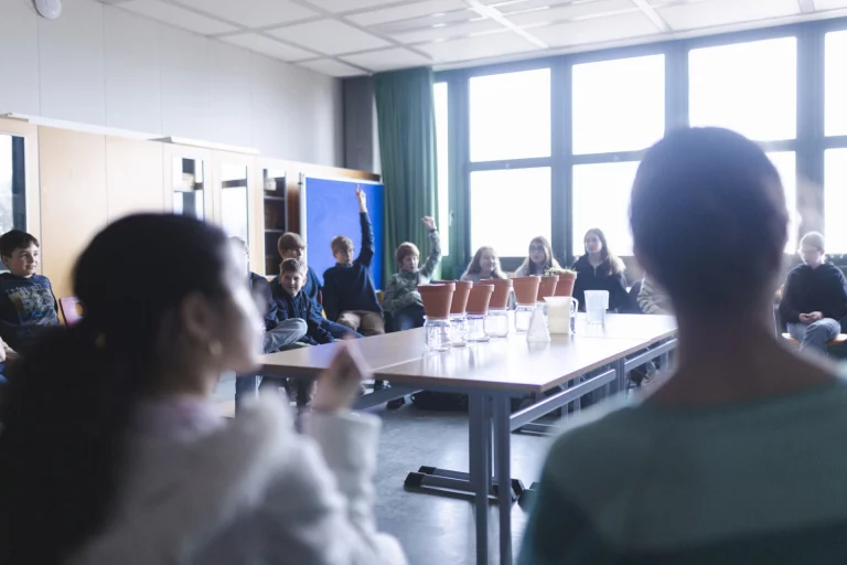 Schulklasse im Klassenzimmer bei einem Experiment zum Klimawandel mit mehreren Gefäßen auf dem Tisch
