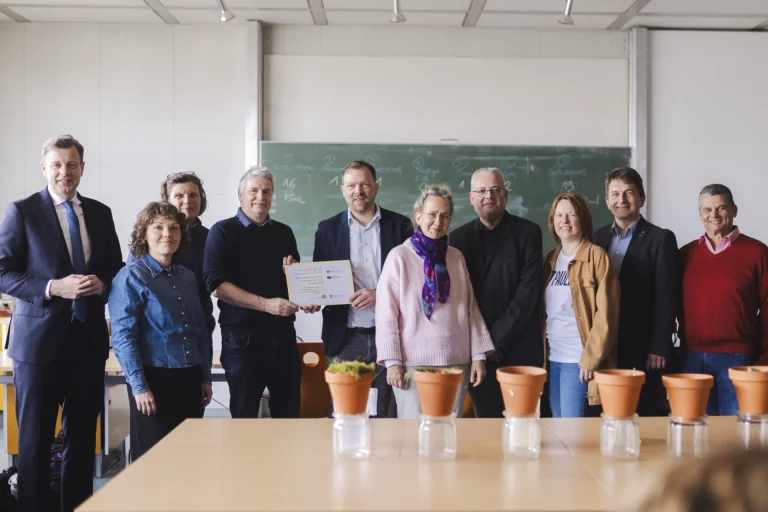 Gruppe von Personen mit Urkunde und Pflanzgefäßen in einem Klassenzimmer