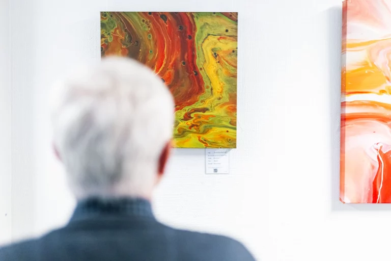Person betrachtet abstraktes Acrylbild in Rot- und Gelbtönen in einer Ausstellung