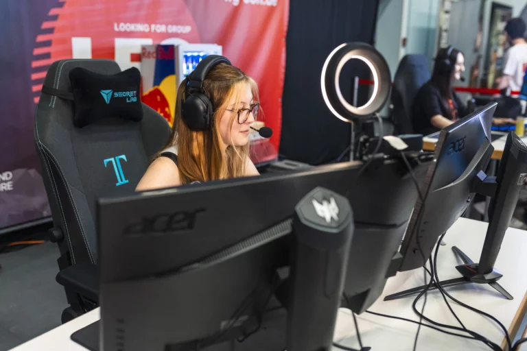 Frau mit Headset und Mikrofon sitzt an Gaming-Monitoren im Messebereich