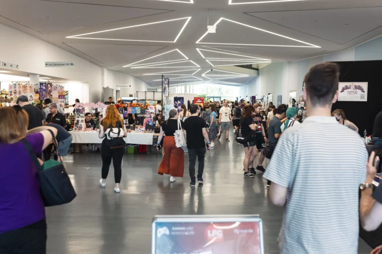 Besucherinnen und Besucher gehen an Messeständen mit Manga- und Gaming-Artikeln entlang
