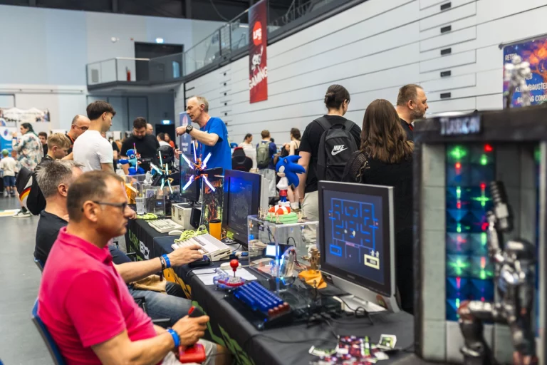 Besucher an Spielautomaten und Retro-Konsolen in einer Messehalle