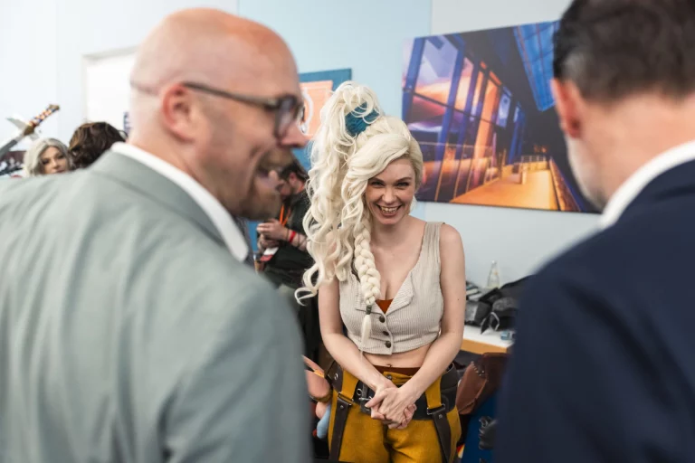 Cosplayerin im Fantasy-Kostüm im Gespräch mit zwei Besuchern im Anzug