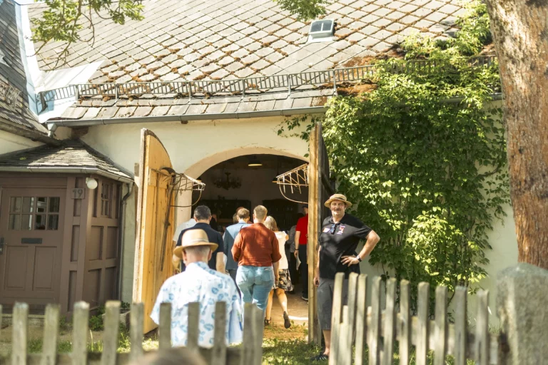Besucherinnen und Besucher betreten eine historische Hofeinfahrt mit Kletterpflanzen während der Dorfbegehung