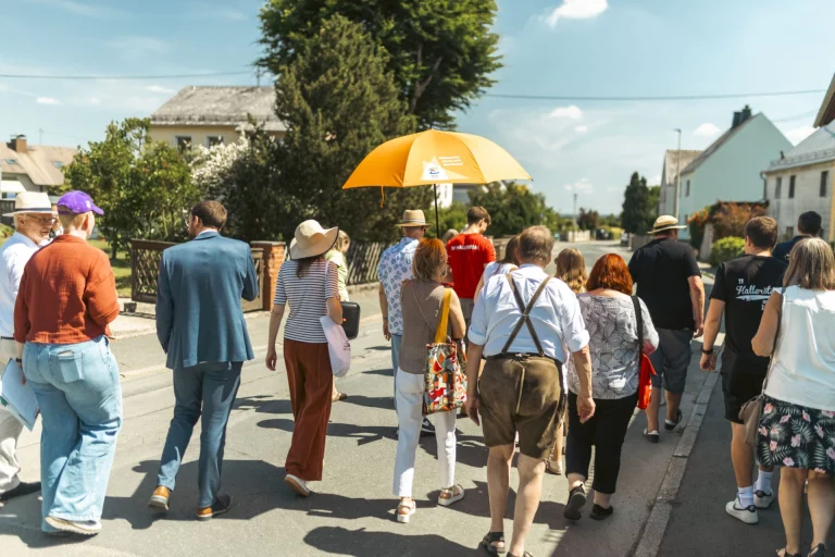 Gruppe von Personen mit gelbem Sonnenschirm geht durch eine Dorfstraße